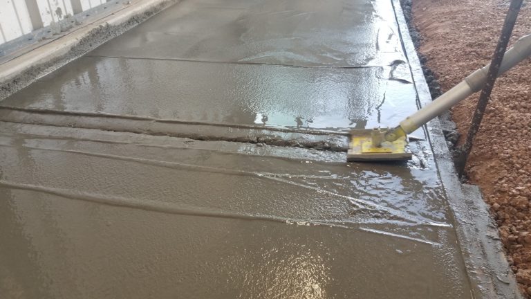 A control joint being put into the concrete using a joint tool with a long handle.