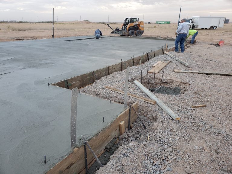 Workers smoothing a freshly poured concrete slab at a construction site.