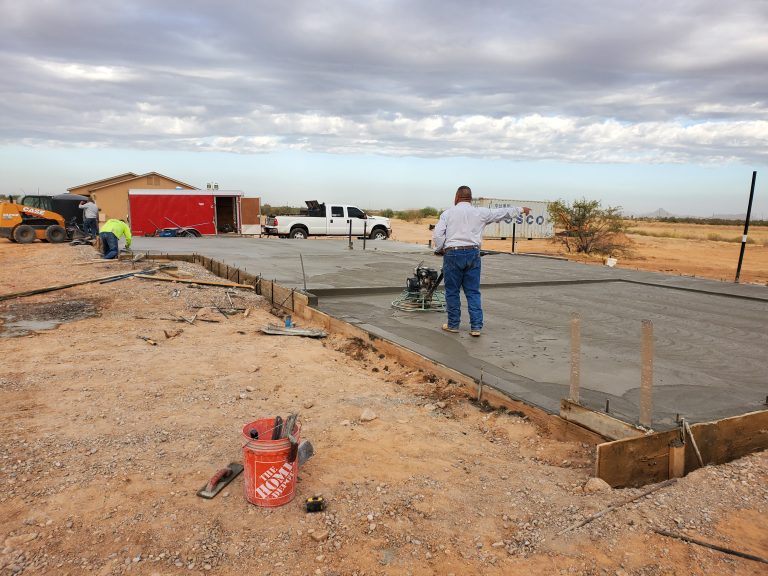 Construction workers finishing a concrete slab foundation in a desert setting.