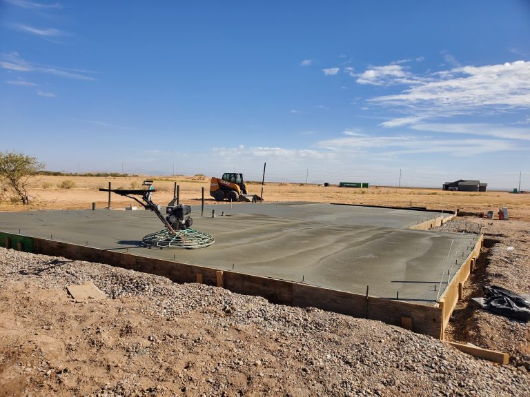 Freshly poured concrete slab curing at a construction site in Coolidge, Arizona, with finishing equipment on the surface.