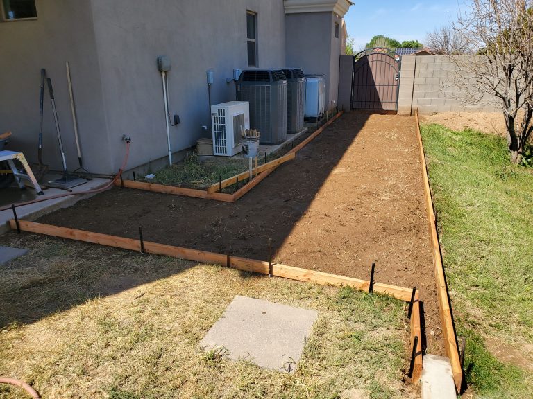 Backyard of a house with wooden concrete forms and excavated dirt ready for a sidewalk pour.