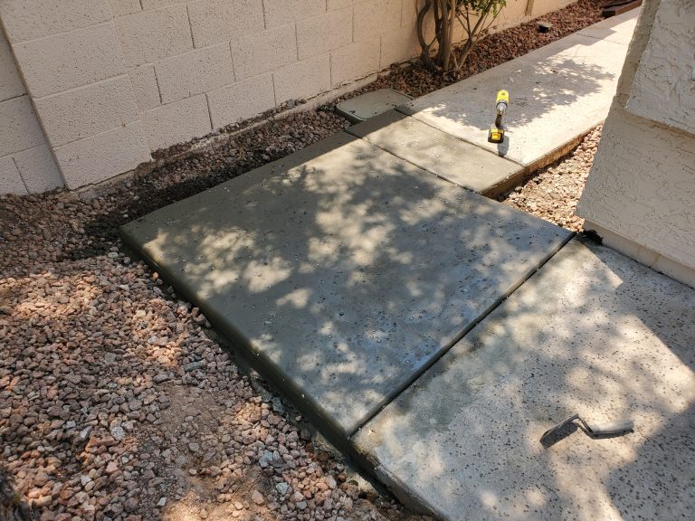 Corner piece of sidewalk with a salt finish, with a few hand tools laying around, the scene covered with the shadow of a tree.