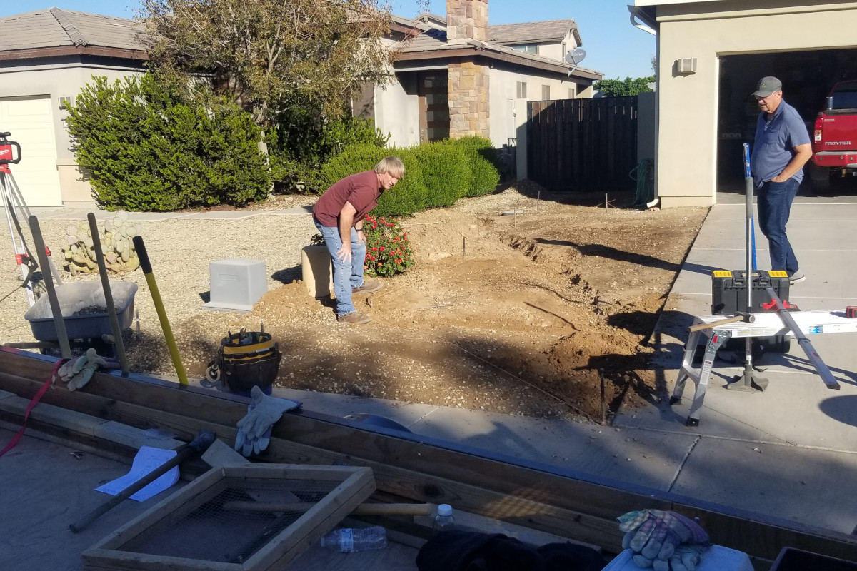Before picture of a concrete crew looking at ground near a driveway that has been disturbed and uneven