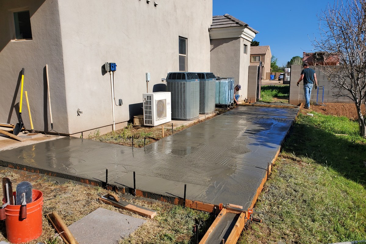 Freshly placed and finished concrete sidewalk addition extending along the side of the home.
