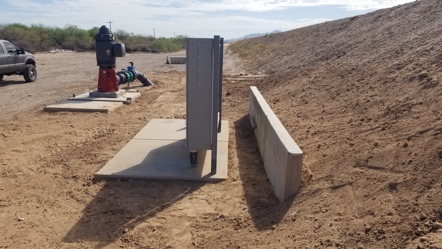 Outdoor industrial equipment beside concrete pads and a low concrete wall